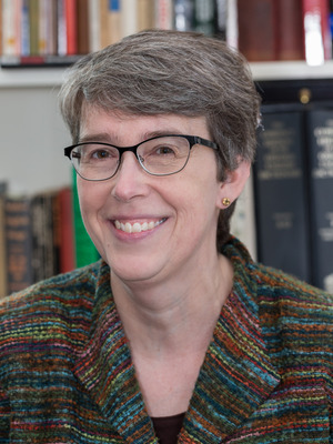 Photograph of woman wearing glasses and striped blazer smiling in front of bookcase