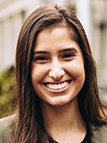 Photograph of smiling woman's face, long brown hair, standing outdoors