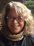 Smiling woman with curly blonde hair and glasses standing outdoors