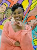 Smiling woman wearing pink flowy dress standing in front of colorful painted wall