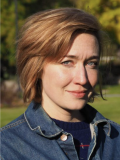 Woman with medium length brown hair outside wearing a jean jacket over a blue shirt