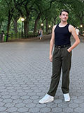 Person standing outdoors wearing a black tank top and green trousers