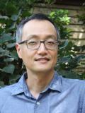 Man with glasses and blue shirt standing in front of brick wall with green foliage