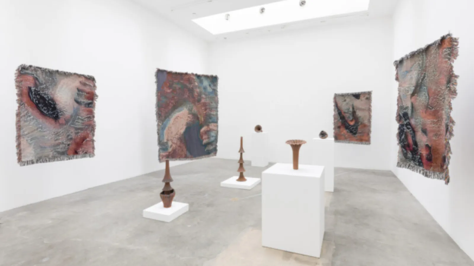 Gallery with large works on walls and several sculptures on white pedestals in center