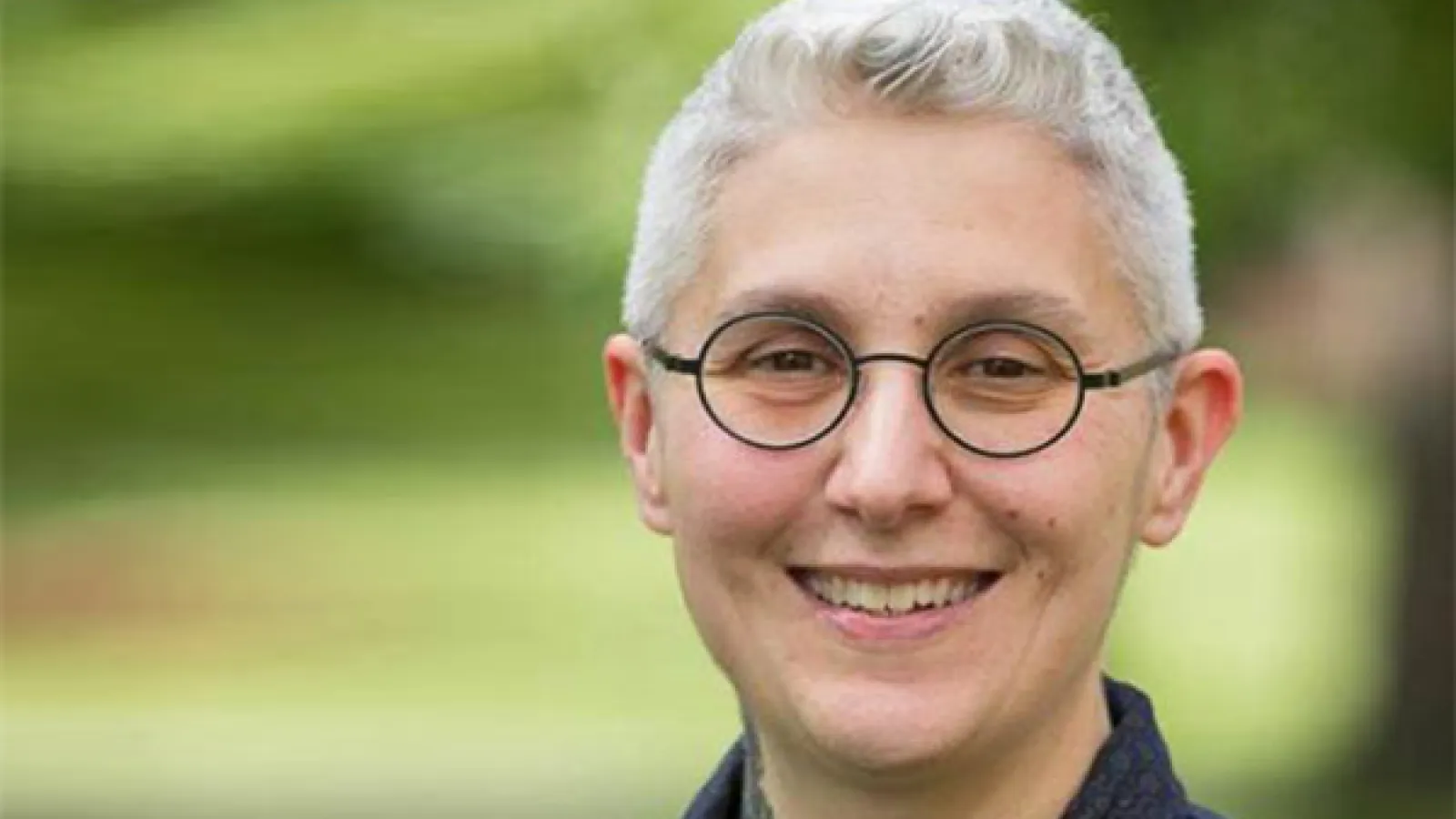 Smiling person with shirt silver hair and round black-rimmed glasses