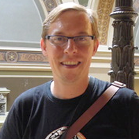Photograph of man with blonde hair wearing a dark tshirt