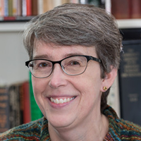Photograph of woman with glasses smiling in front of bookshelves