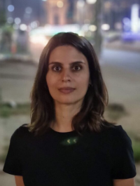 Woman with long dark hair and dark shirt standing outside in a city