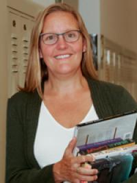 Smiling woman with long blonde hair holding a stack of books