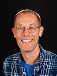 Smiling man with short hair, glasses and a blue shirt