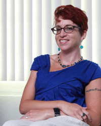 Photograph of a smiling woman with short red hair wearing glasses and a blue blouse