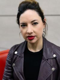 Woman with dark hair wearing a dark shirt and motorcycle jacket