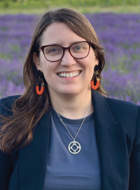 Smiling woman with long hair and glasses standing in field of purple flowers