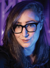 Smiling woman with glasses and dark hair with purple backdrop