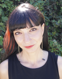 Smiling woman with long dark hair standing in front of green foliage