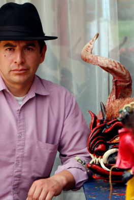 Photograph of man in red shirt wearing a black hat next to sculptures