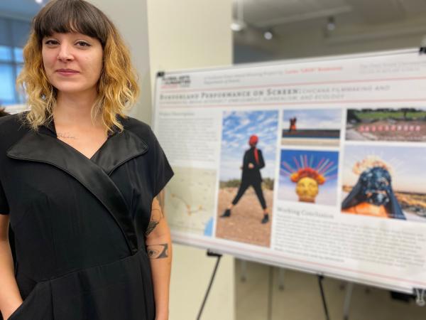 Photograph of graduate student in front of their research poster