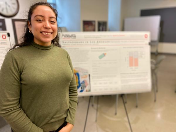 Photograph of graduate student in front of their research poster