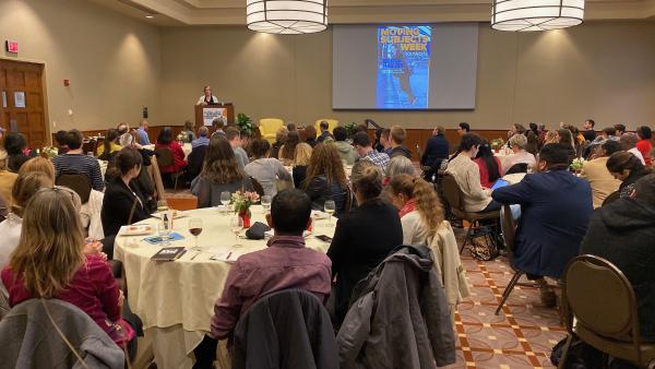 Photograph of Becca Heller speaking to crowded ballroom