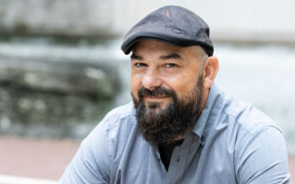 Smiling man with a beret hat, dark beard and mustache and light shirt