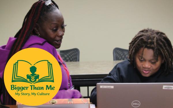 An adult woman helps a young boy write on a laptop
