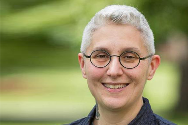 Smiling person with shirt silver hair and round black-rimmed glasses