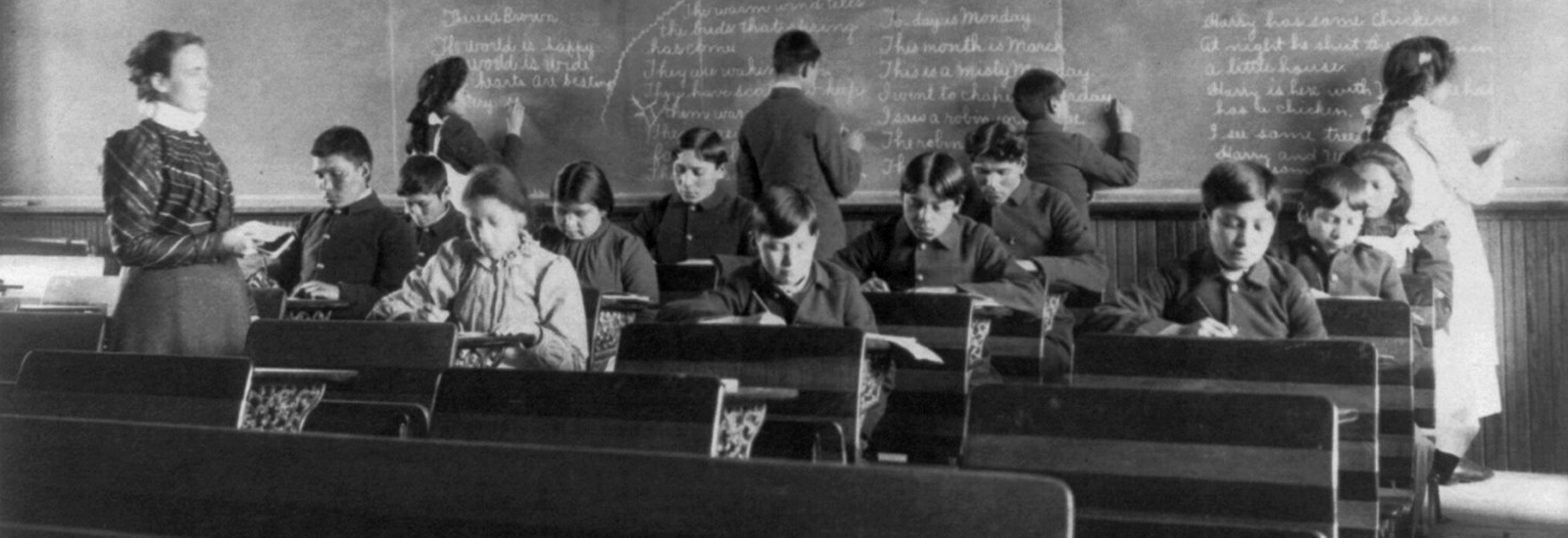 Students in an English class, some seated and some writing on a chalkboard