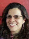 Smiling woman with dark hair and glasses in front of a red brick wall