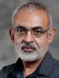 Serious man with silver hair and beard and glasses