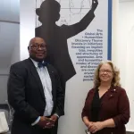 Two people stand in front of an event sign